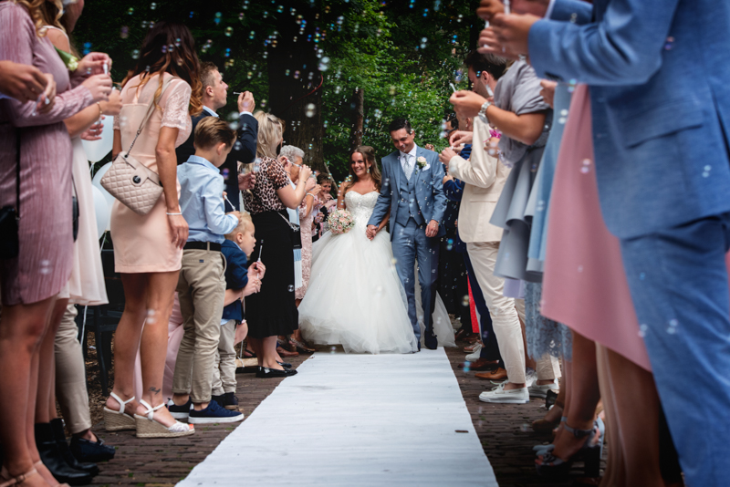 Het bruidspaar wat toegejuicht wordt na de ceremonie met bellenblaas en een haag van mensen
